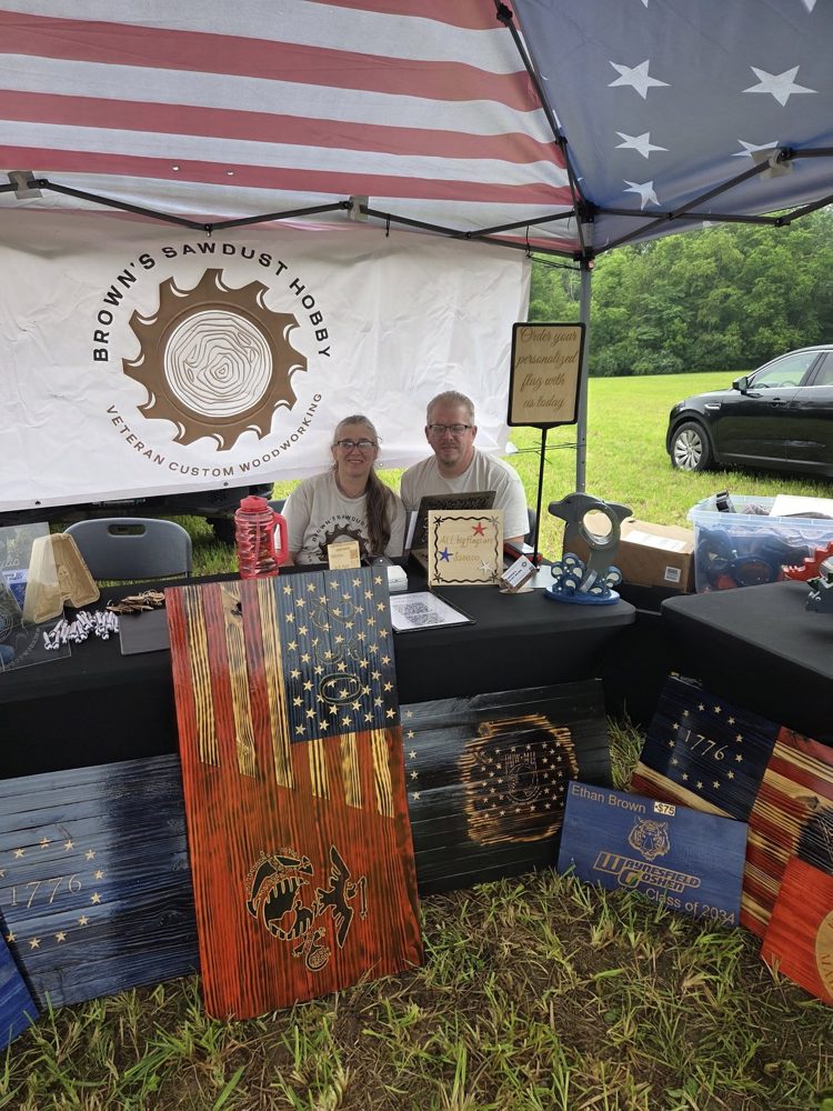 Andrew and Peggy behind the Brown's Sawdust Hobby booth under the flag tent